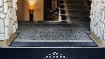 A hotel entrance with a stone wall, a black doormat with the name 'villa eugenia', and a staircase leading to the upper floor.