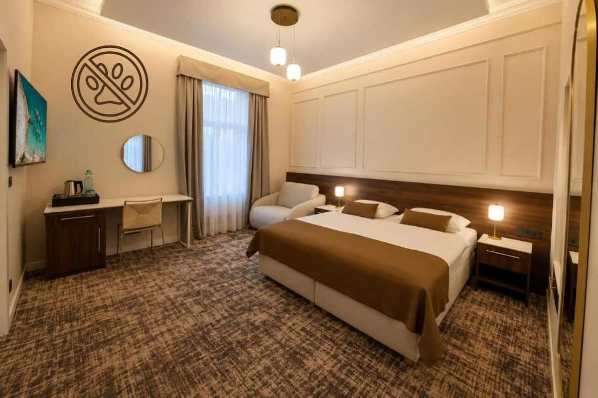 Habitación de hotel con cama, escritorio, silla, espejo y ventana con cortinas.