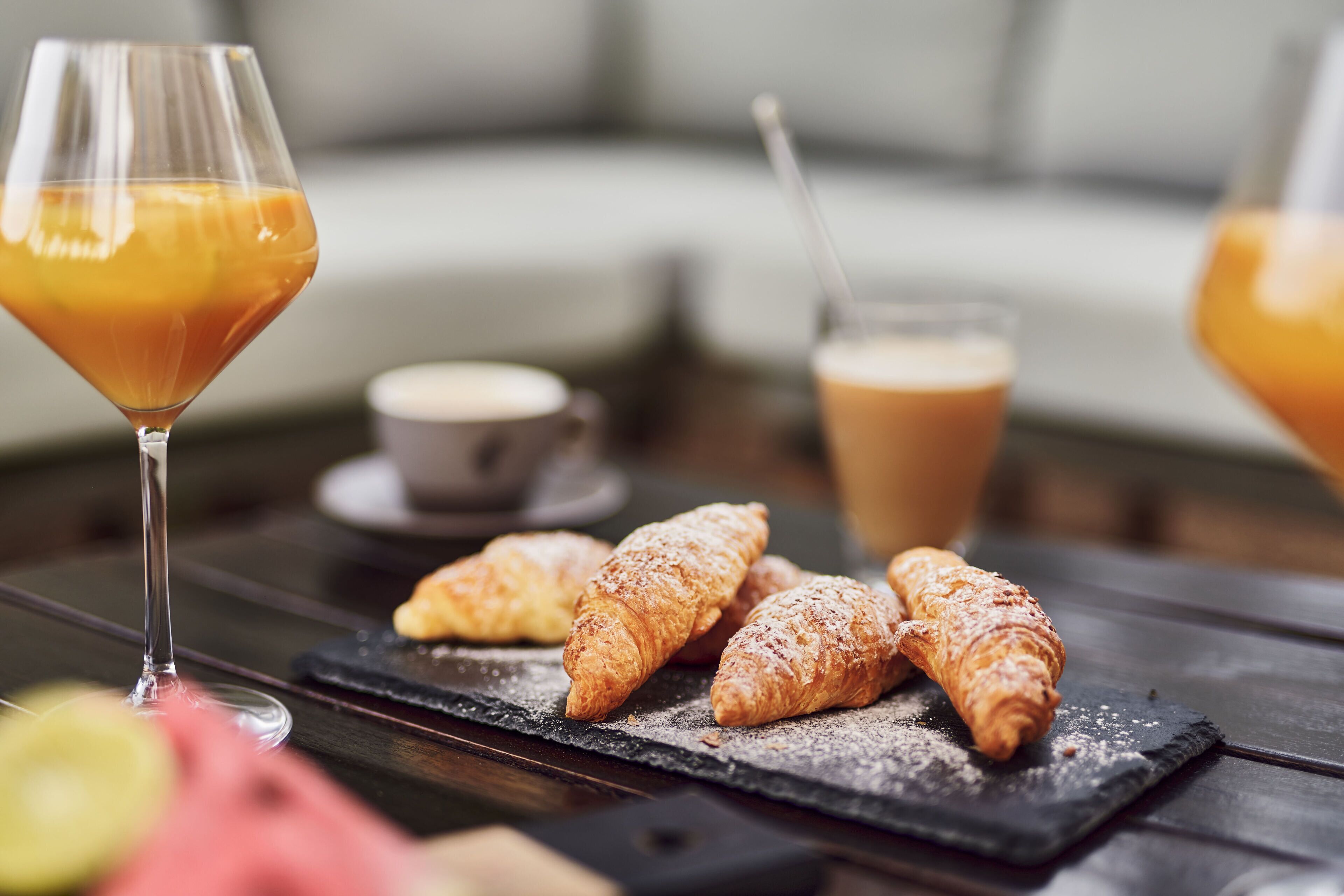 Una mesa con cruasanes, un vaso de jugo de naranja y una taza de café.