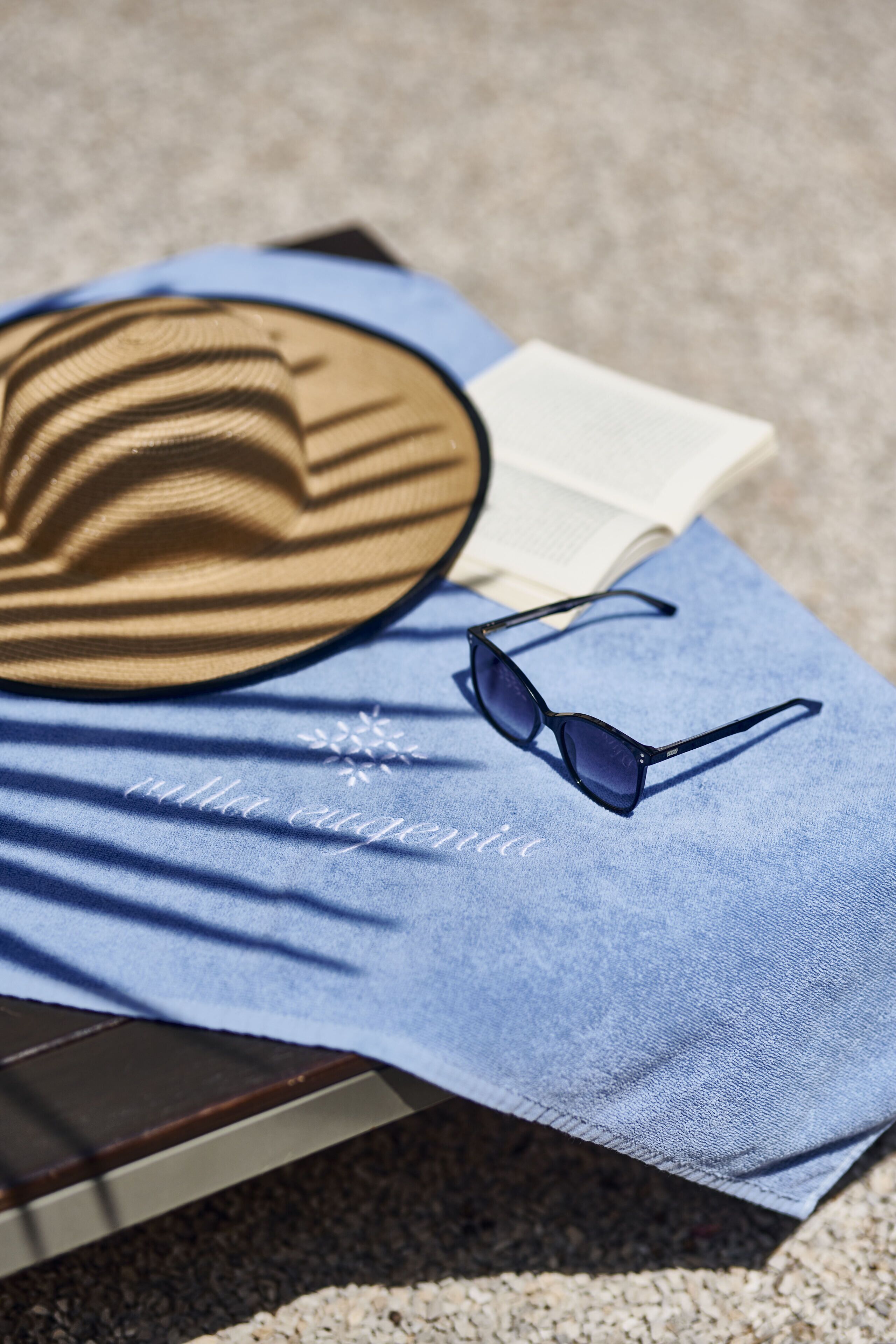 A hat, sunglasses, and a book on a blue cloth.