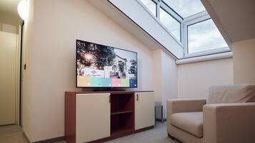 A modern living room with a flat-screen TV on a wooden cabinet, a beige sofa, and a skylight above.