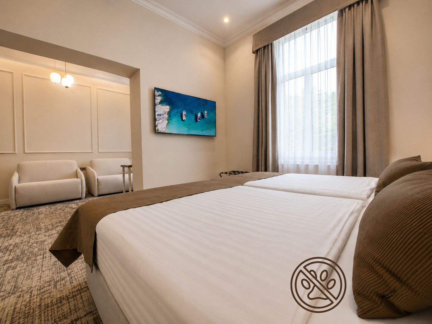 A hotel room with a large bed, two armchairs, a painting of a beach, and a window with curtains.