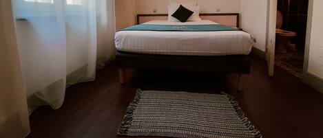 Una cama bien hecha con un plaid verde, un cuadro en la pared y vistas al baño a través de una puerta abierta.