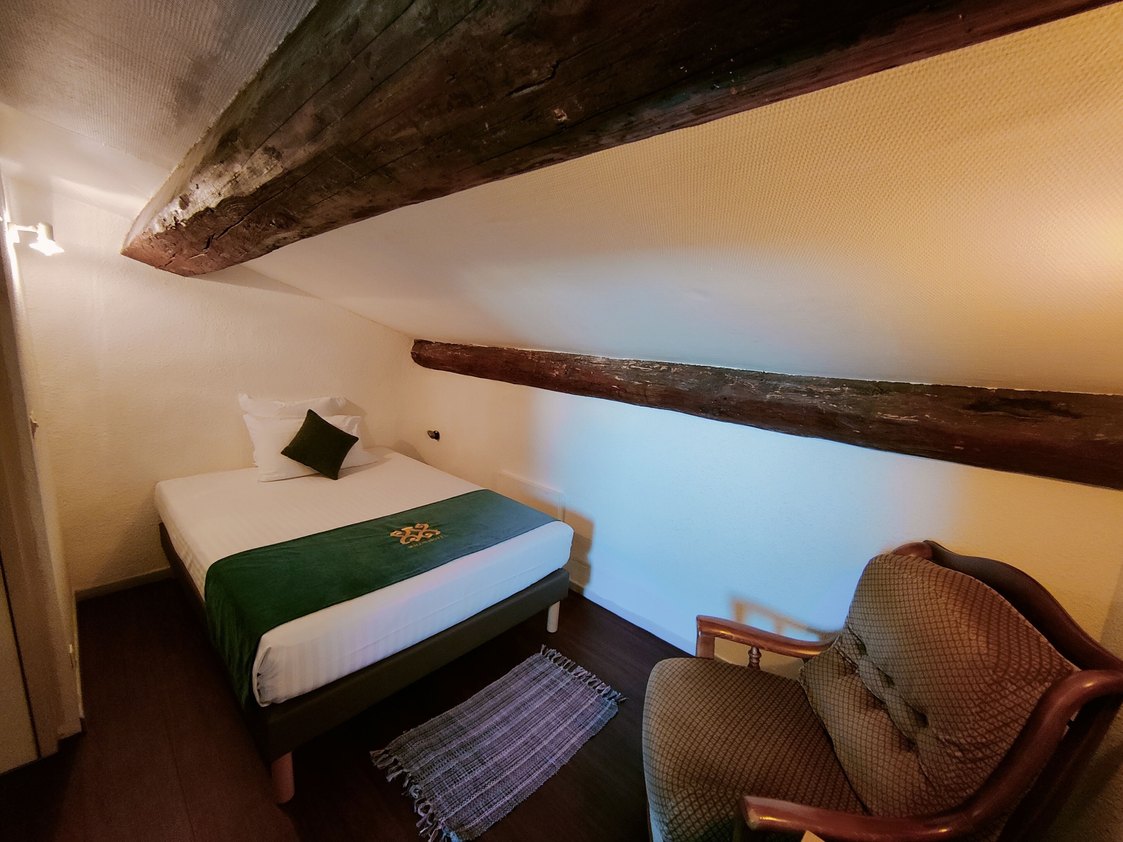 Una habitación pequeña y acogedora con una cama individual, una silla y techo con vigas de madera.