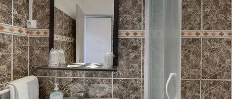 A bathroom with a marble-tiled wall, a white sink with a soap dispenser, a mirror above the sink, and a towel hanging on a rack.