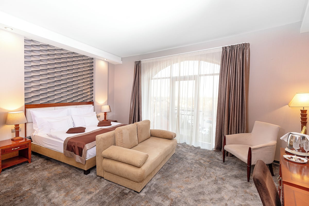A hotel room with a bed, a sofa, a chair, a desk, and a window with curtains.