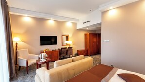 A hotel room with a bed, two sofas, a desk with a lamp, a TV, and a wardrobe. - Colosseum Hotel Mórahalom (Morahalom)