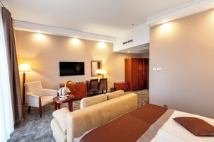 Habitación de hotel con cama, dos sofás, escritorio con lámpara, televisión y armario.