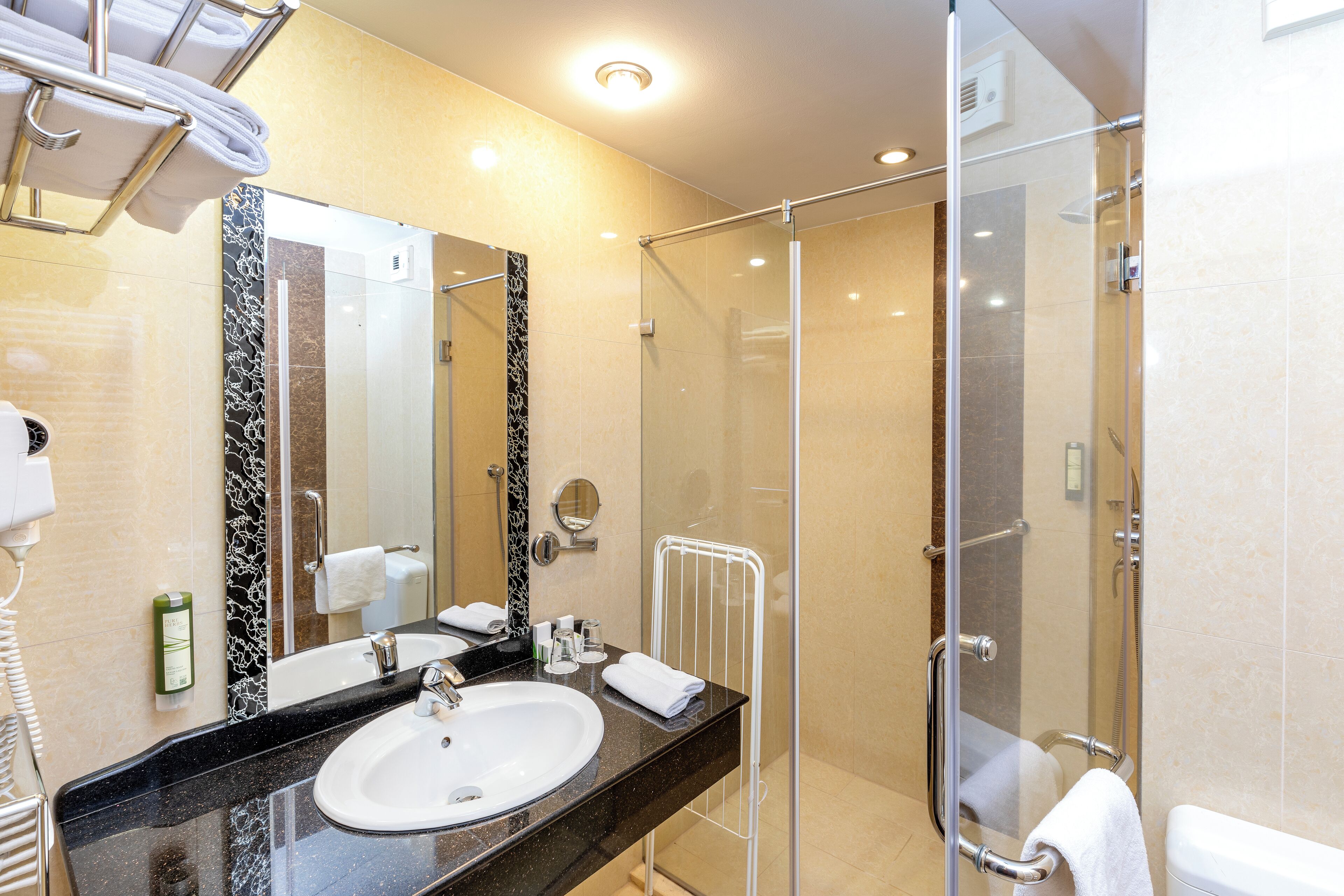 Un baño moderno con ducha envuelta en vidrio, un lavamanos con encimera de mármol y un espejo grande.
