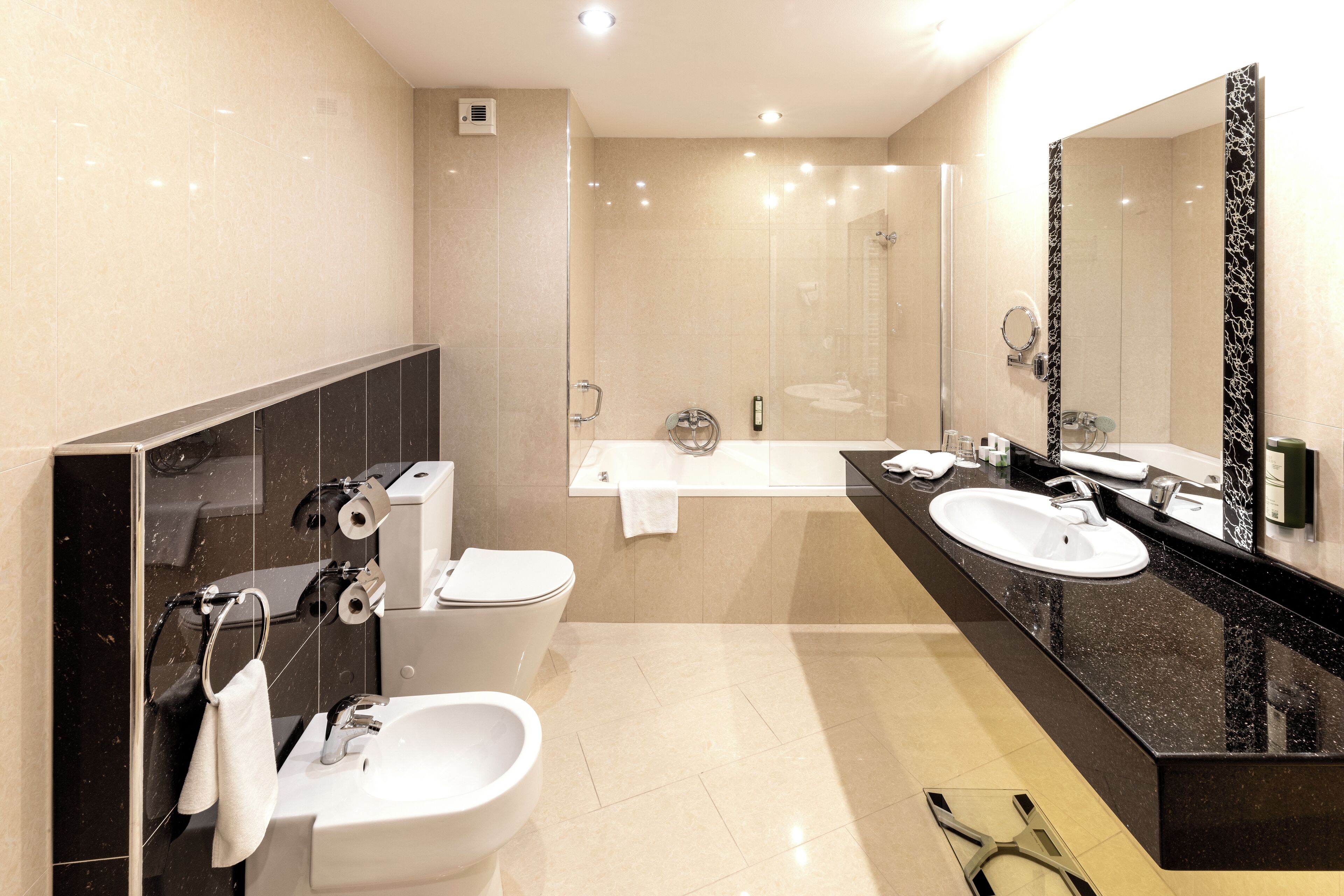 Un baño moderno con encimera negra, lavamanos blanco y un espejo grande.