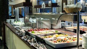 A buffet with various food options, including salads, meats, and desserts, with serving utensils and plates arranged on the counter. - Colosseum Hotel Mórahalom (Morahalom)