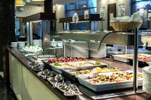 Un bufé con diversas opciones de comida, incluyendo ensaladas, carnes y postres, con utensilios y platos dispuestos en la barra.