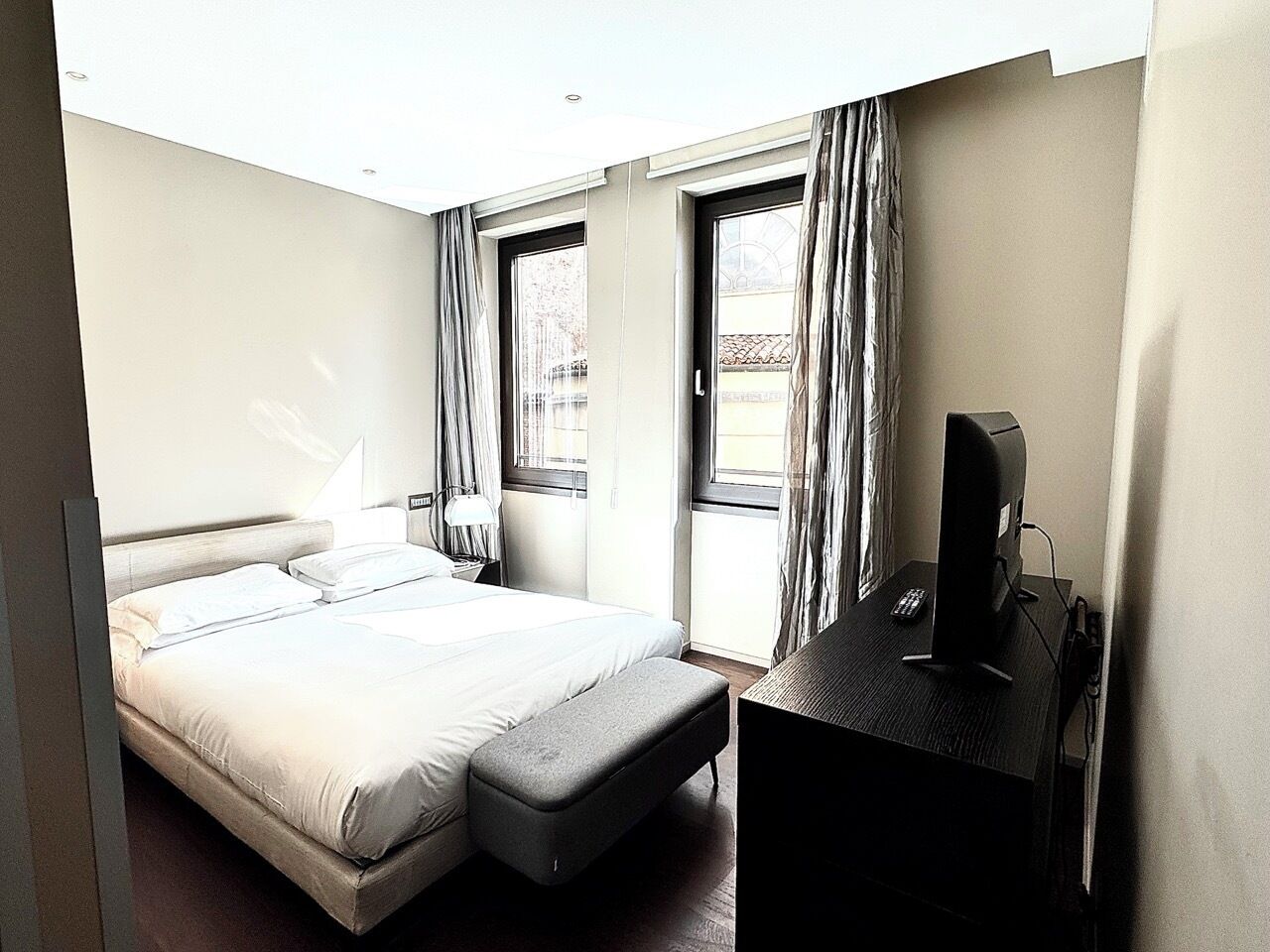A hotel room with a bed, a desk with a computer, and a window with curtains.