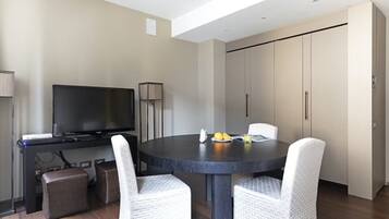 Een moderne hotelkamer met een ronde eettafel, twee witte fauteuils, een flatscreen televisie, een minibar en een grote inbouwkast.