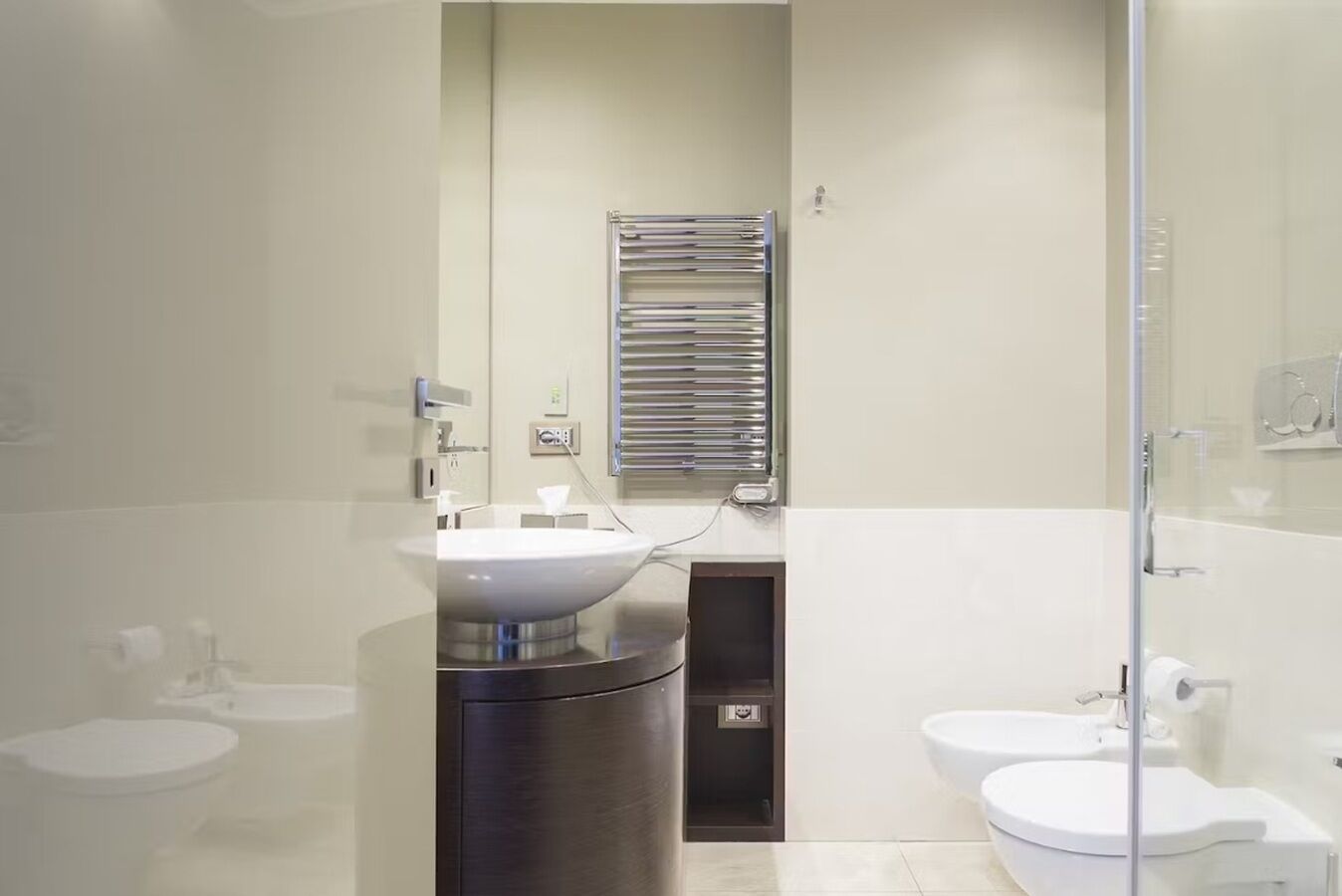 A modern bathroom with a large sink, two toilets, a mirror, and a towel rack.