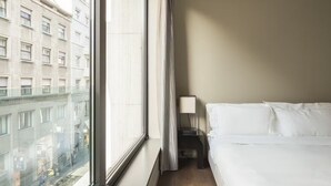 Ett hotellrum med ett stort fönster, en säng och ett nattduksbord med en lampa.