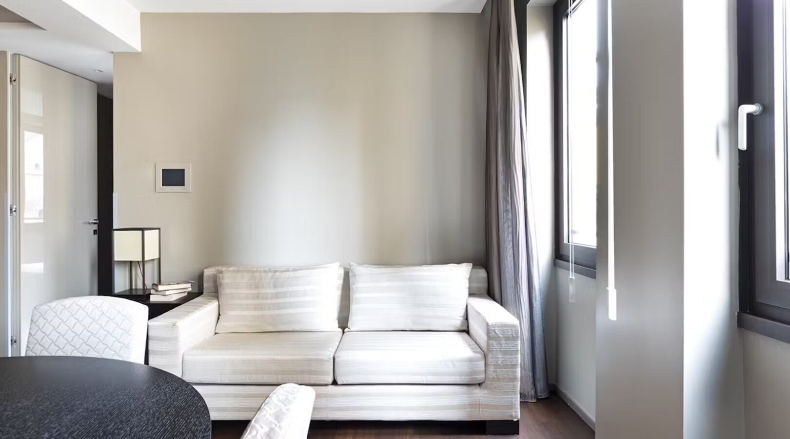 Un salon moderne avec un canapé, une petite table, une lampe et une vue sur l’extérieur.