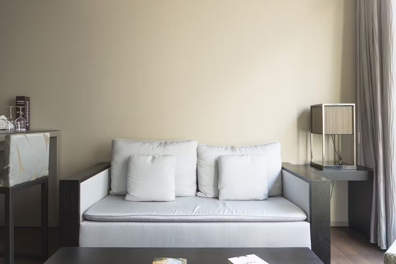 A modern hotel room with a sofa, a small table, a lamp, and a curtain.