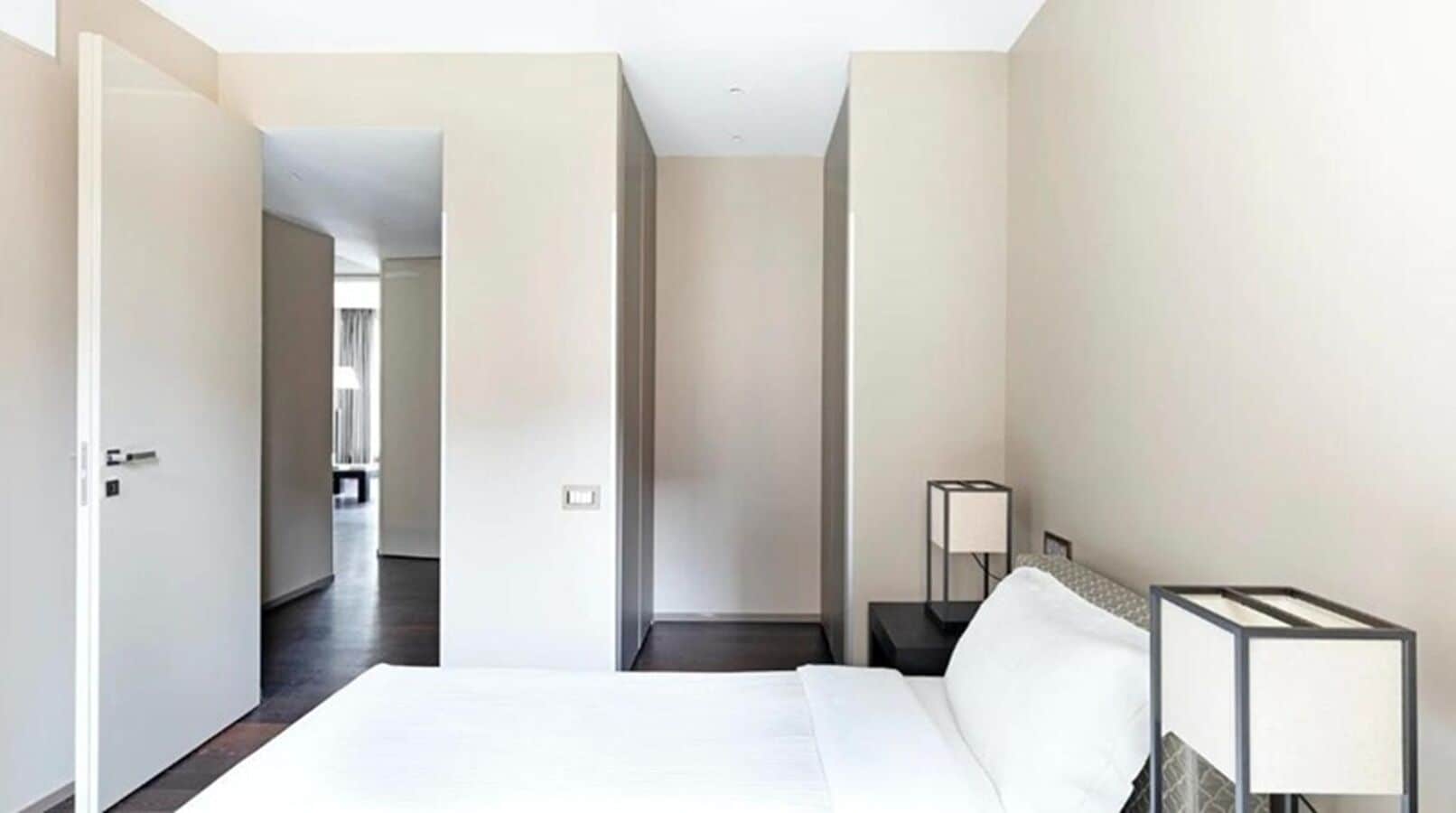 A hotel room with a bed, bedside tables, a lamp, and a view of a hallway.