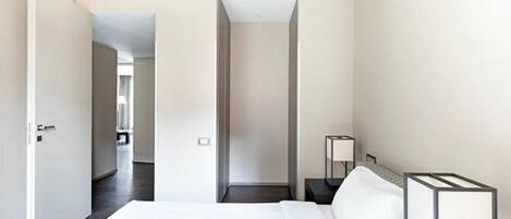 A hotel room with a bed, bedside tables, a lamp, and a view of a hallway.