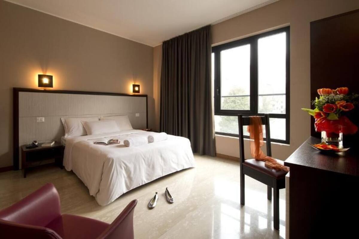 A hotel room with a large bed, a desk, a chair, and a window with curtains.