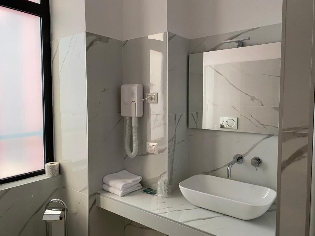 A modern bathroom with a marble sink, a handheld showerhead, and a towel rack.
