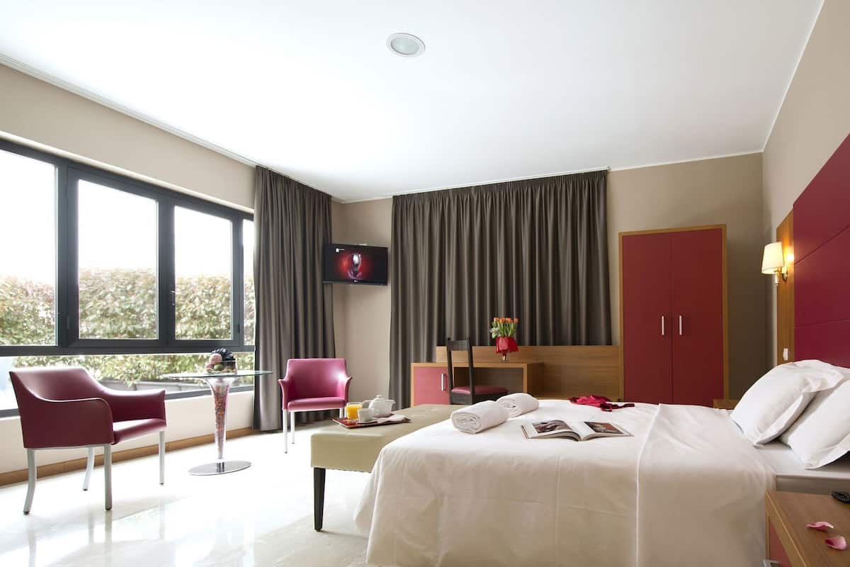 A modern hotel room with a bed, a desk, a chair, a TV, and a wardrobe.