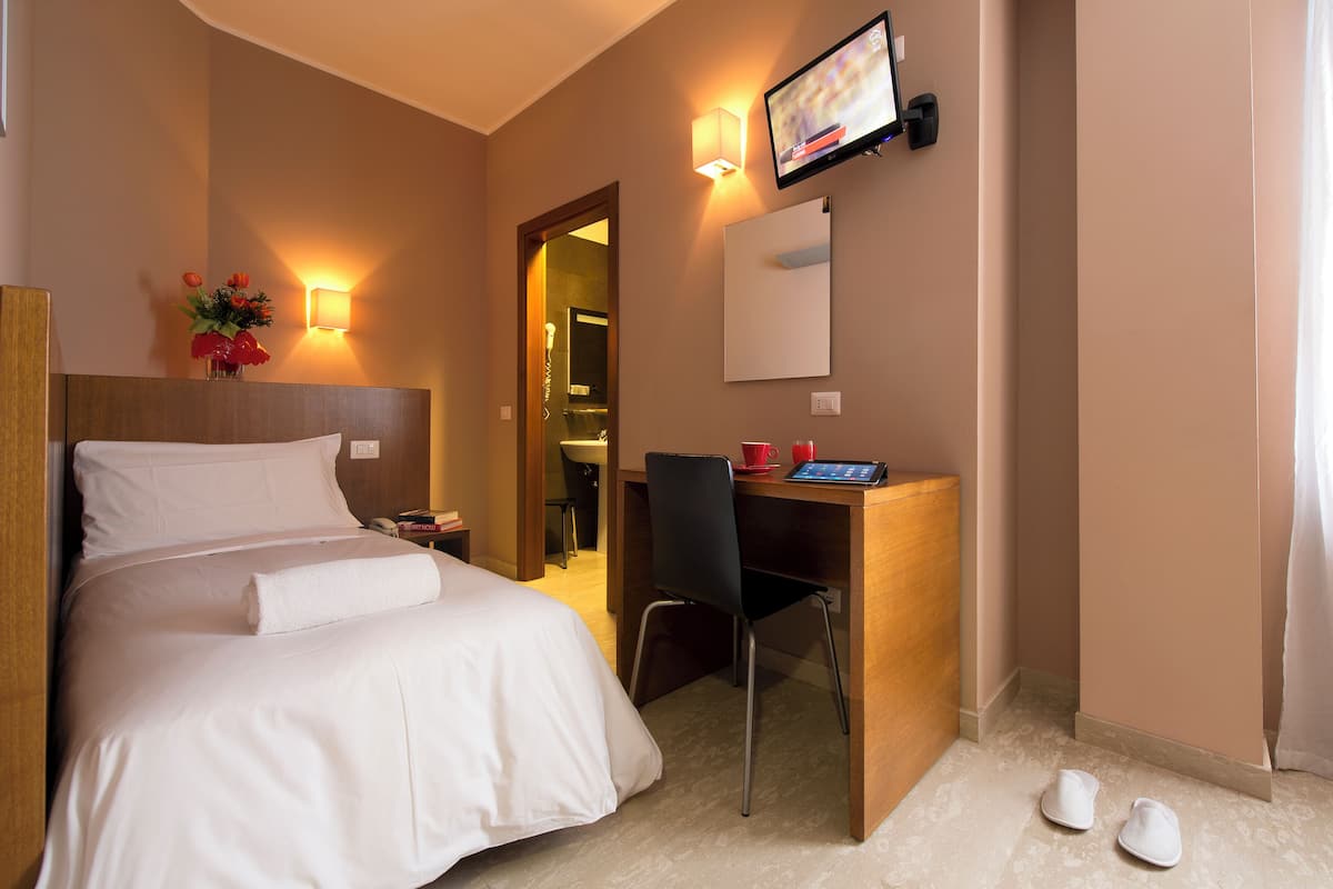 A hotel room with a bed, a desk with a chair, a TV, and a bathroom visible through an open door.