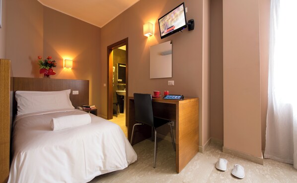 A hotel room with a bed, a desk with a chair, a TV, and a bathroom visible through an open door. - Oasi Village Hotel (Milan)