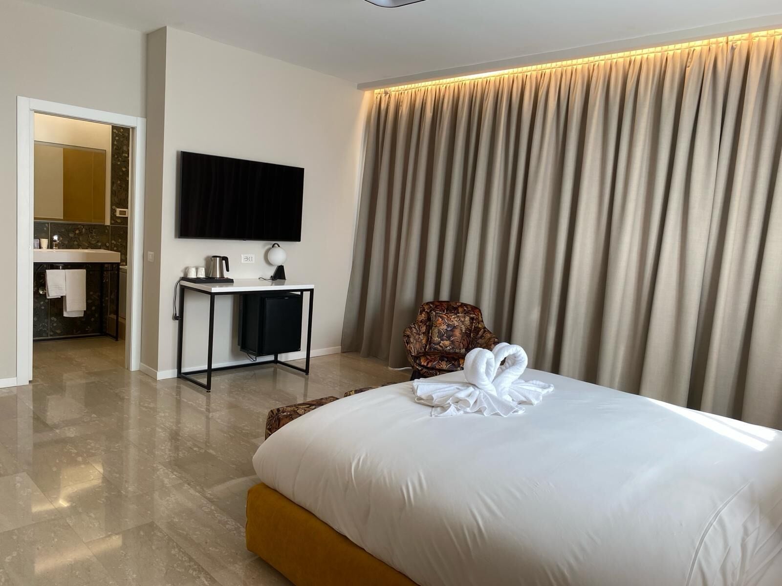 Ein Hotelzimmer mit einem Bett, einem Schreibtisch mit Flachbildfernseher, einem Sessel und einem durchgegangenen Tür erkennbaren Badezimmer.