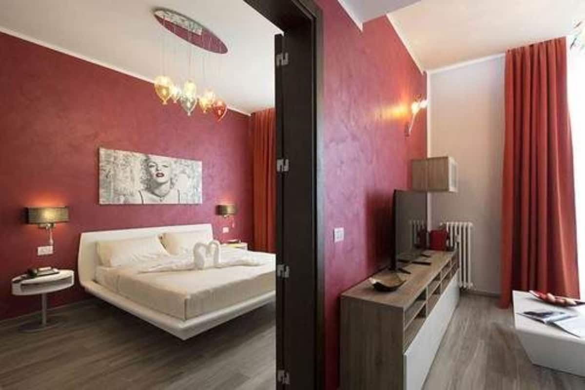 A modern bedroom with a bed, bedside tables, a TV, and a red accent wall.