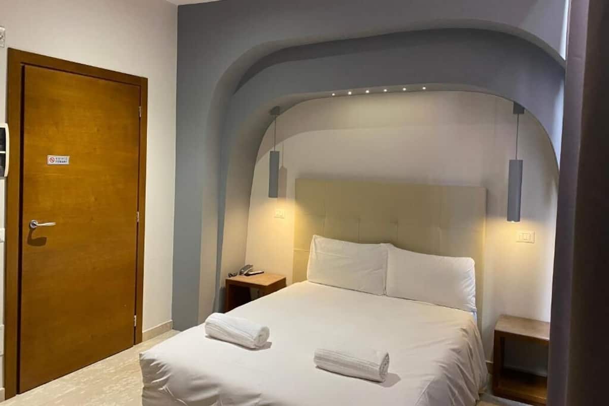 A hotel room with a large bed, a wooden door, and a nightstand with a phone.