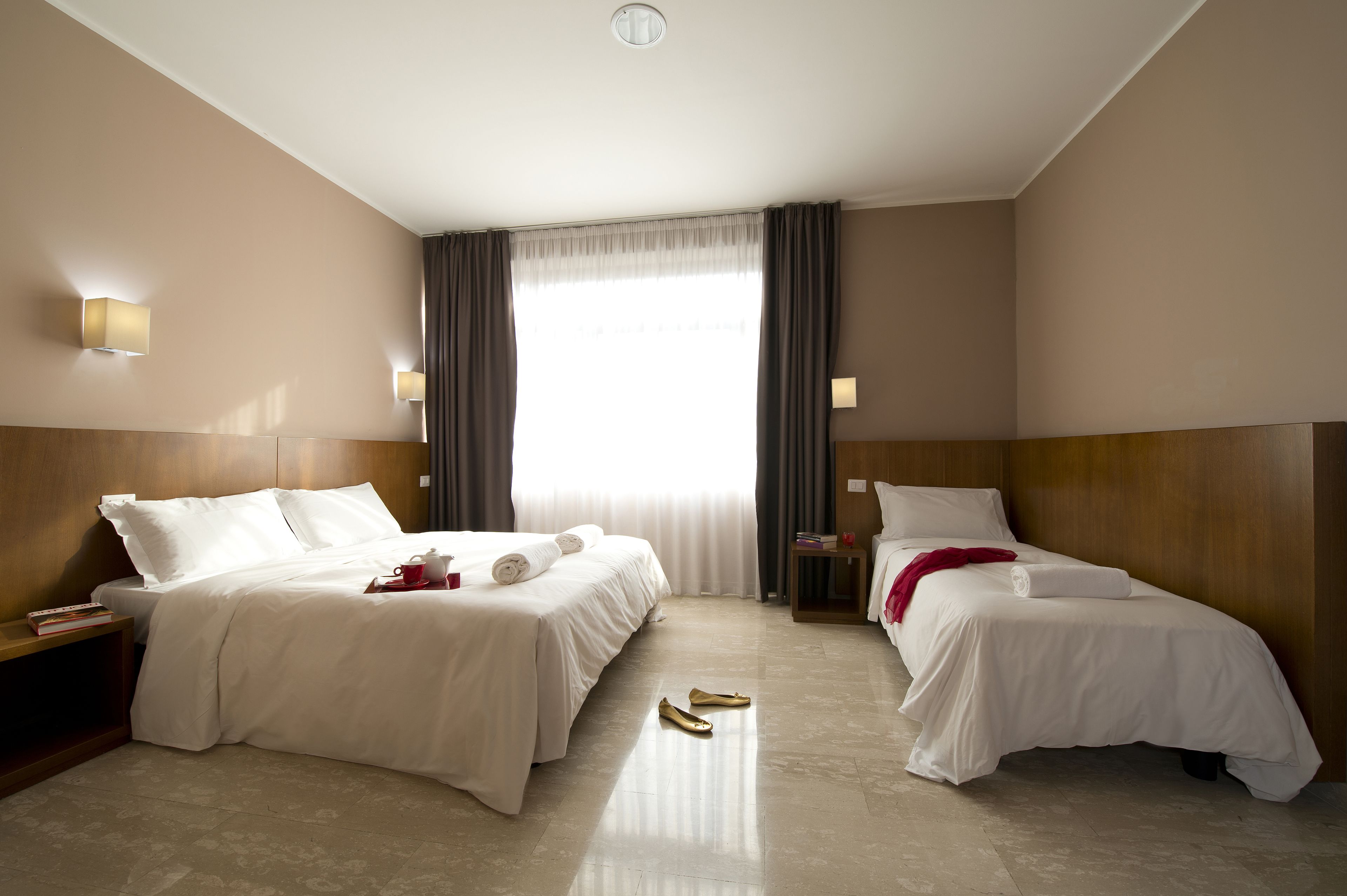 Una habitació d'hotel amb dos llits, una finestra gran amb cortines i un panell de capçalera de fusta.