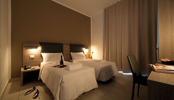 Una camera d'albergo con due letti, una scrivania con una sedia, un telefono e una bottiglia di champagne sul comodino.