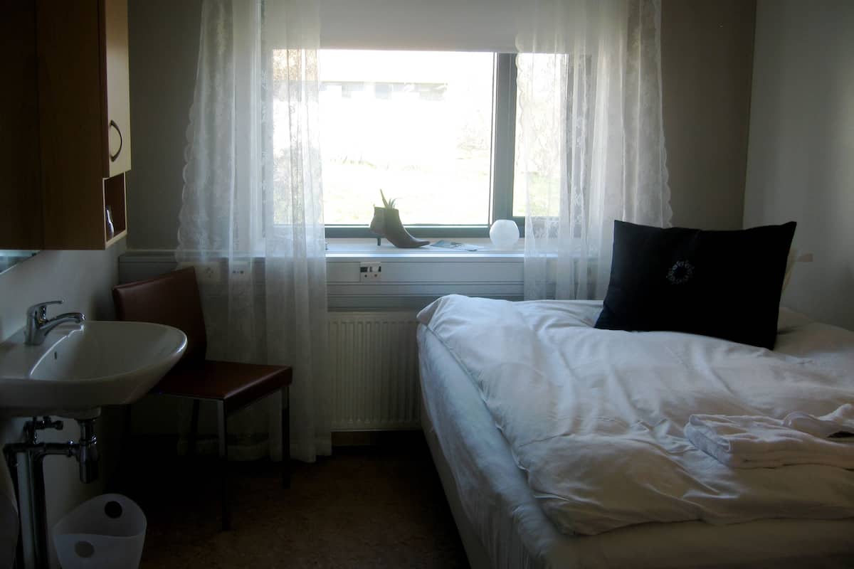 A bedroom with a bed, a window with a view, a chair, a sink, and a cabinet.