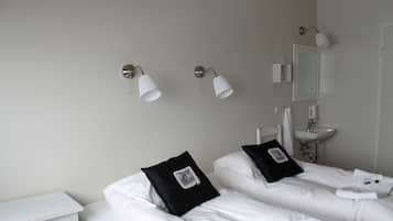 A hotel room with two beds, a nightstand, a white dresser, a wall-mounted sink, and two wall sconces.