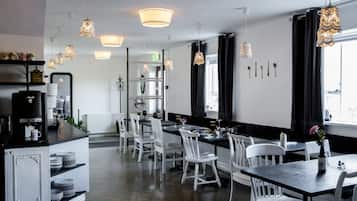 A modern dining area with white chairs and tables, pendant lights, and a kitchen counter with appliances.