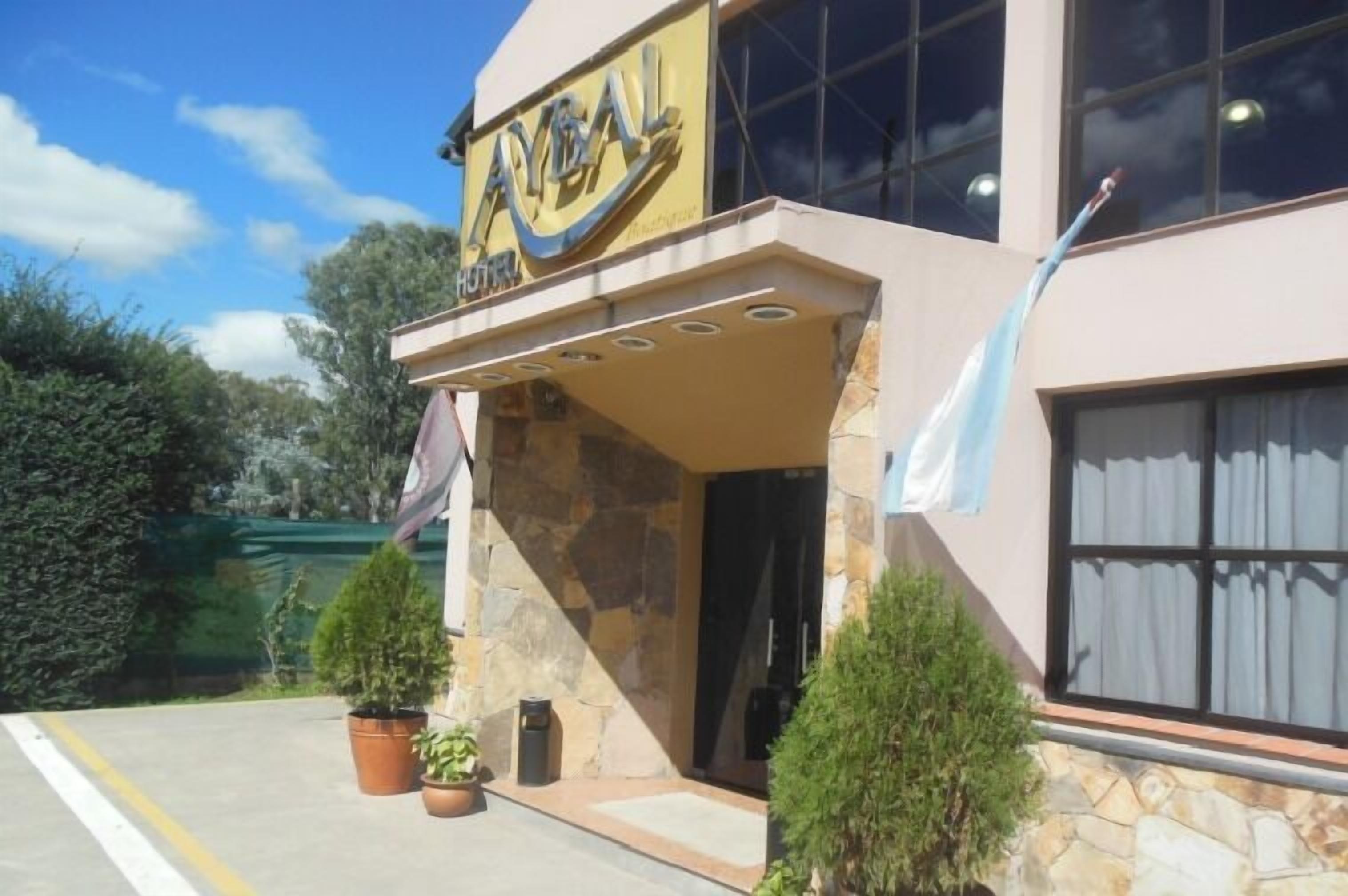 A hotel named "AYAL" with a stone facade, large windows, and a well-maintained entrance area with potted plants.