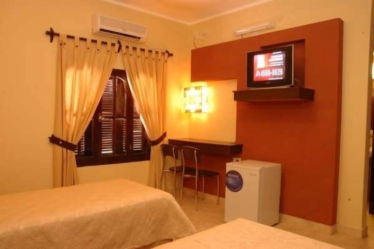 A hotel room with two beds, a desk, a television, and a washing machine.