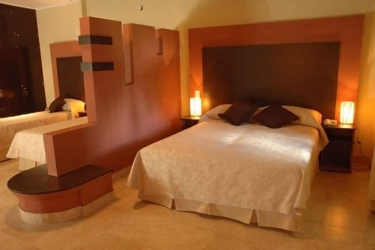 A hotel room with a large bed, two bedside tables, a curved bench, and a modern wall design.