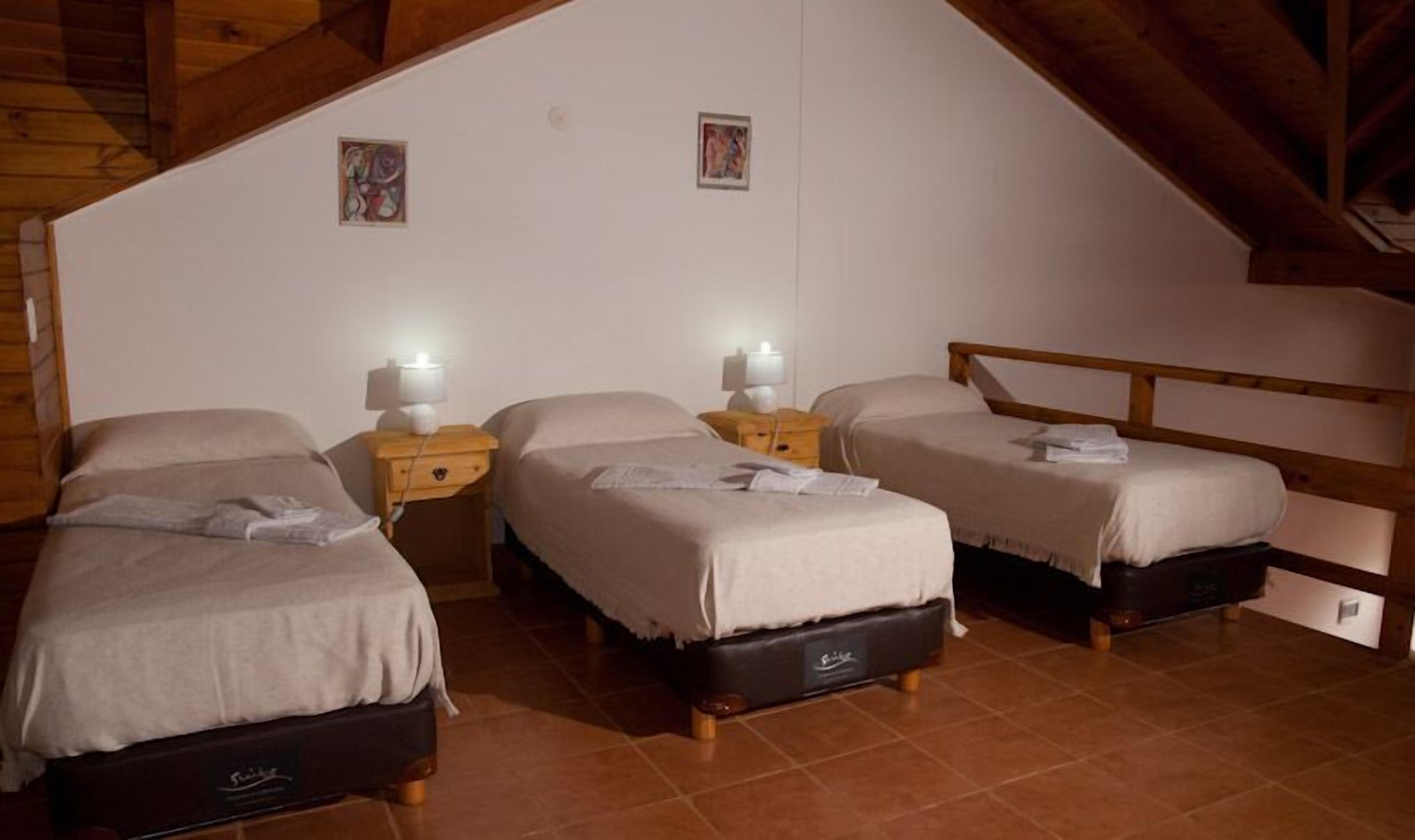 A room with three single beds, wooden nightstands with lamps, and a sloped ceiling.