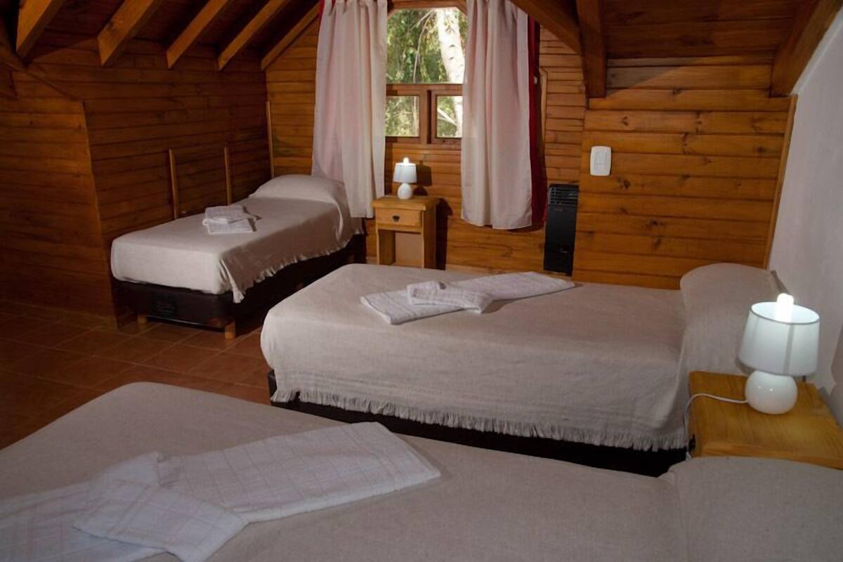 A cozy cabin with two beds, a small table with a lamp, and a window with curtains.