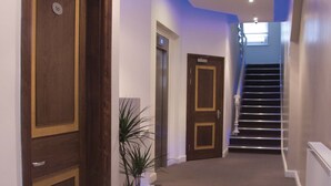 A hallway with wooden doors, a potted plant, and a staircase leading to an elevator. - NOX HOTELS - Notting Hill (London)