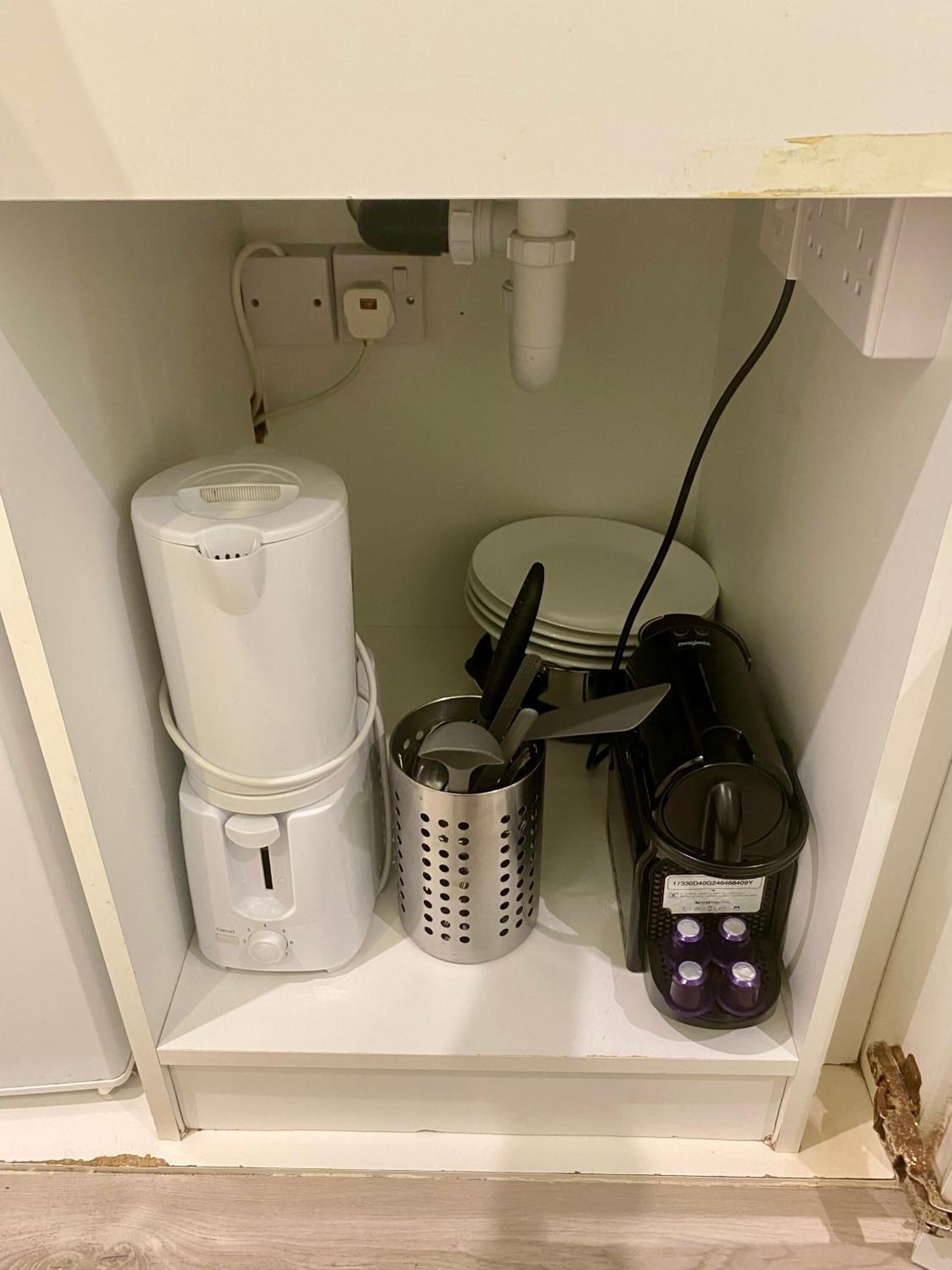 A kitchen shelf with a coffee maker, a food processor, a colander, a stack of plates, and a blender.