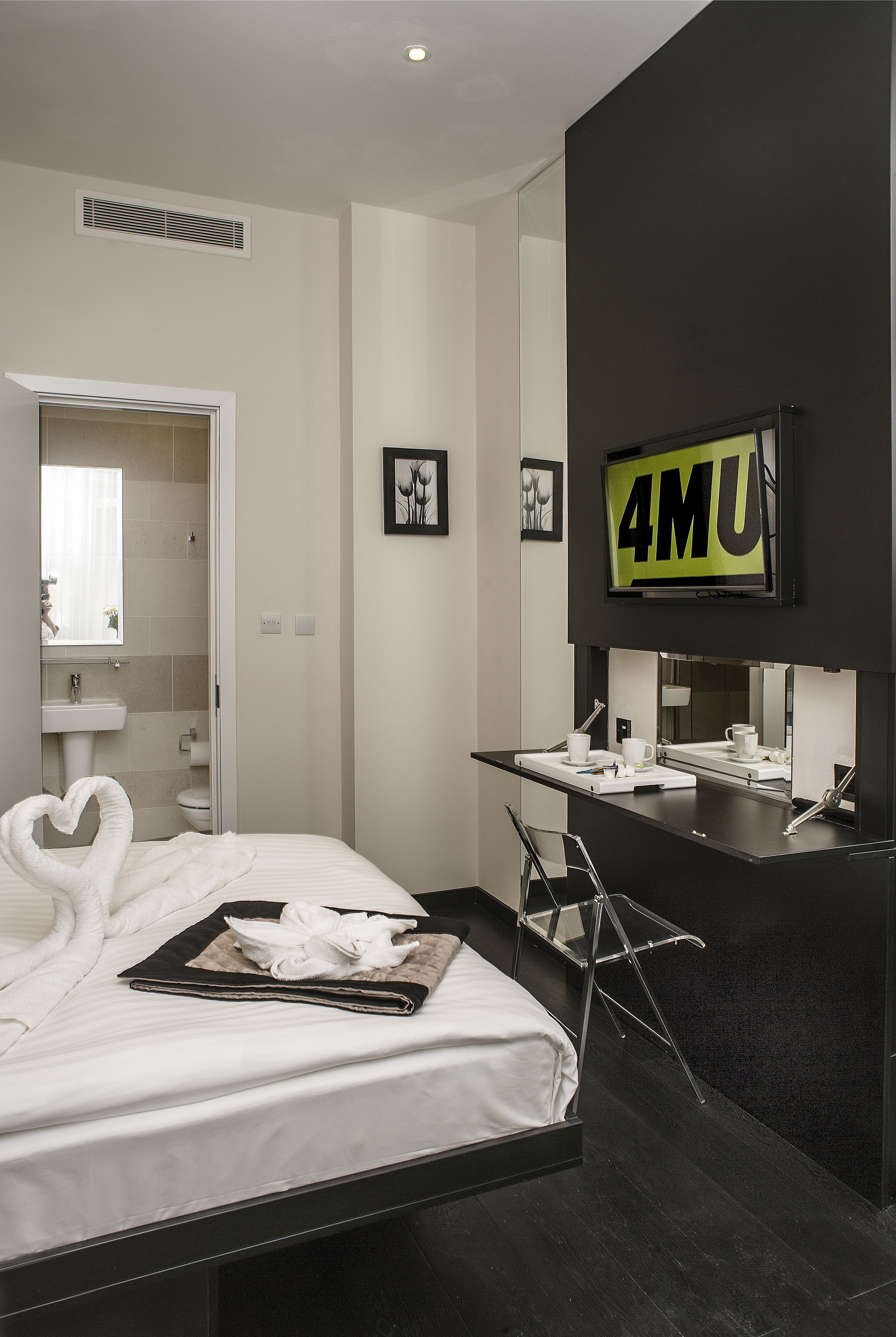 A modern hotel room with a bed, a desk, a sink, and a mirror.