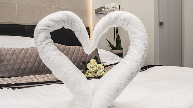 A bed with a heart-shaped towel arrangement and a bouquet of white roses. - NOX HOTELS - Notting Hill (London)