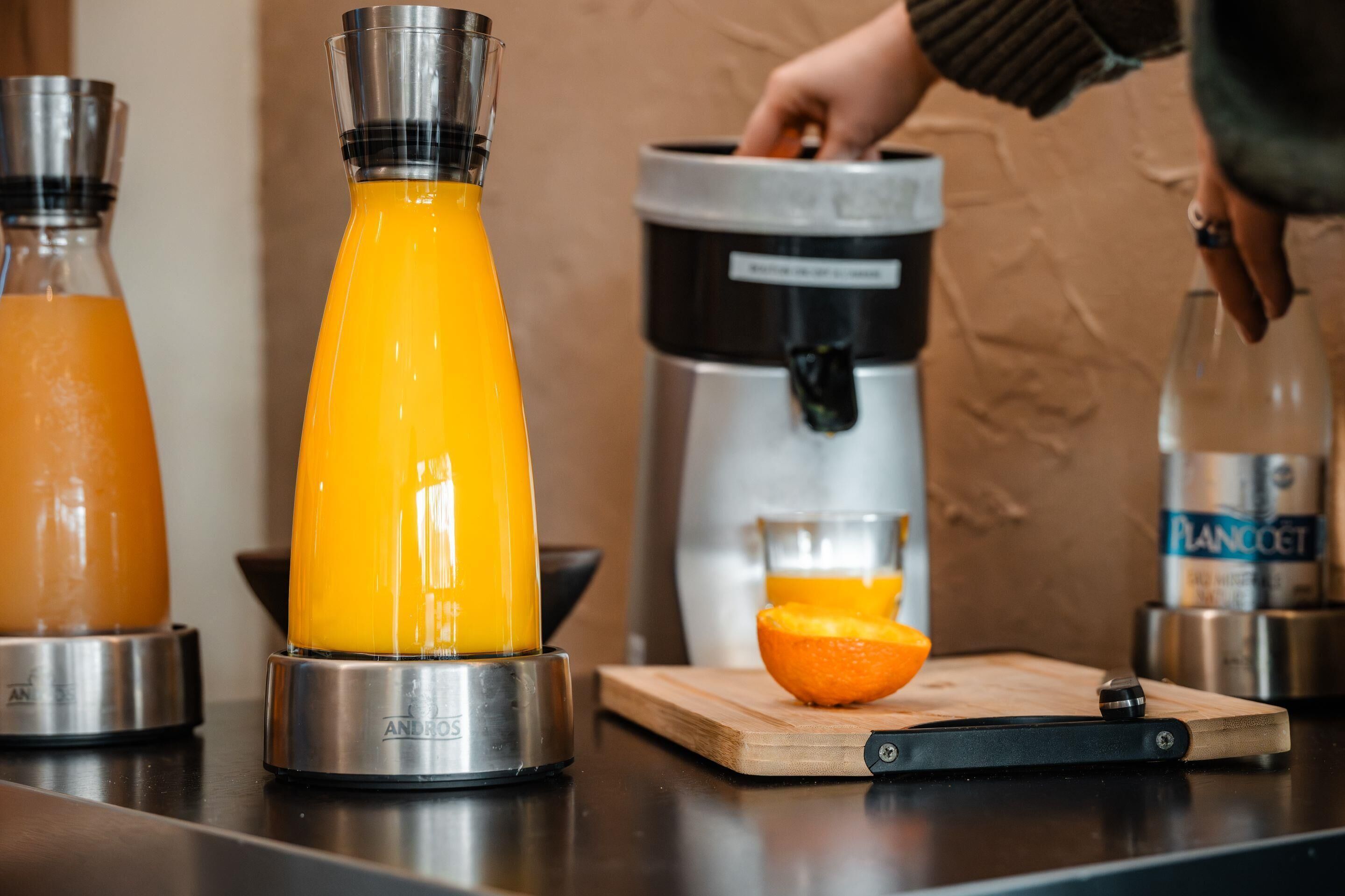 Una cocina con licuadora, cafetera y tabla de cortar con una naranja encima.