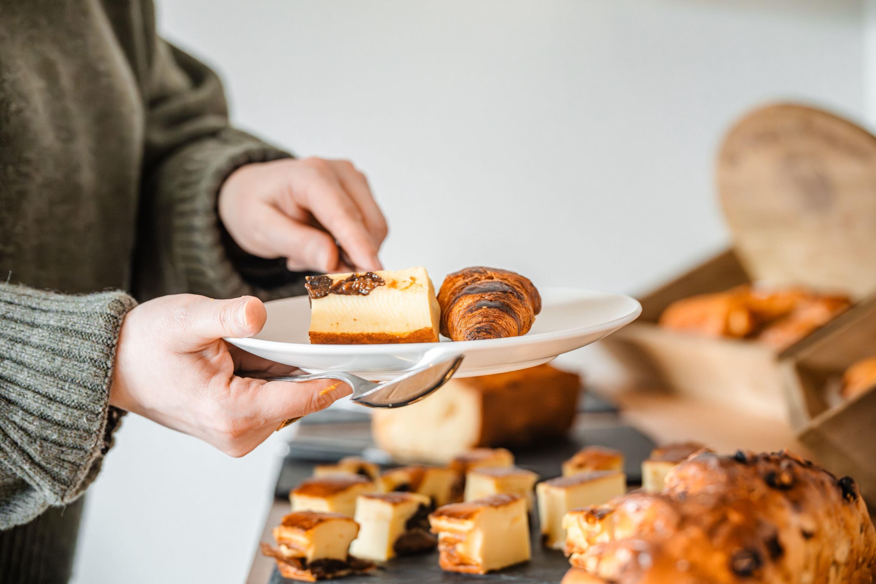 En person som håller i en tallrik med ett bakverk och en bit cheesecake.