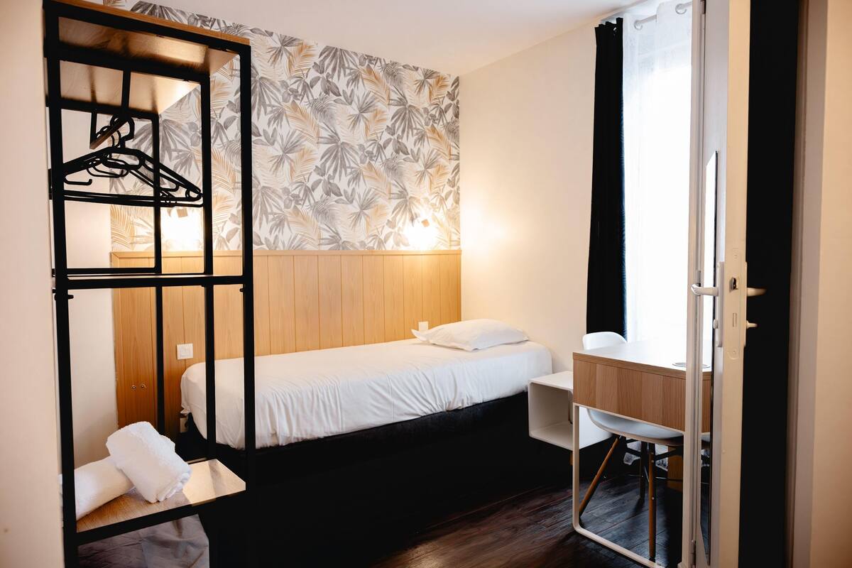 A compact bedroom with a bed, a desk, and a hanging clothes rack.