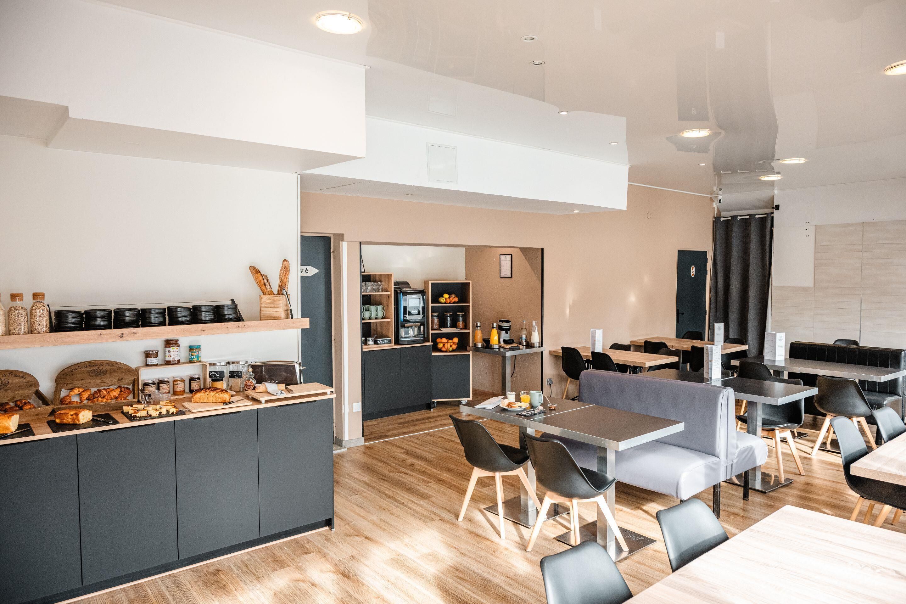 Un café moderno con un mostrador central que exhibe pasteles y bebidas, zonas de estar con mesas y sillas, y una cocina al fondo.